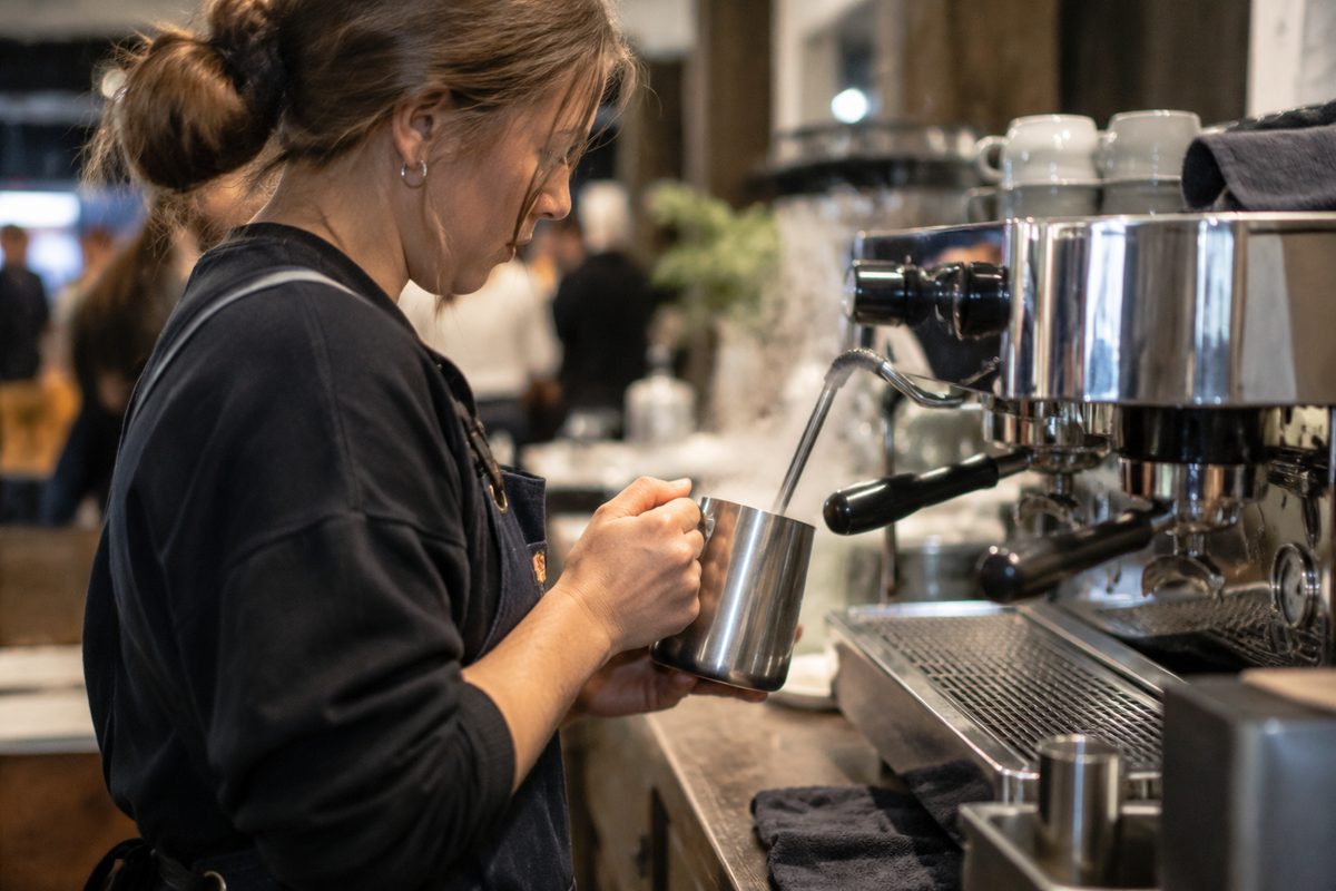 Barista aerating microfoam milk in a stainless steel pitcher at the event espresso station